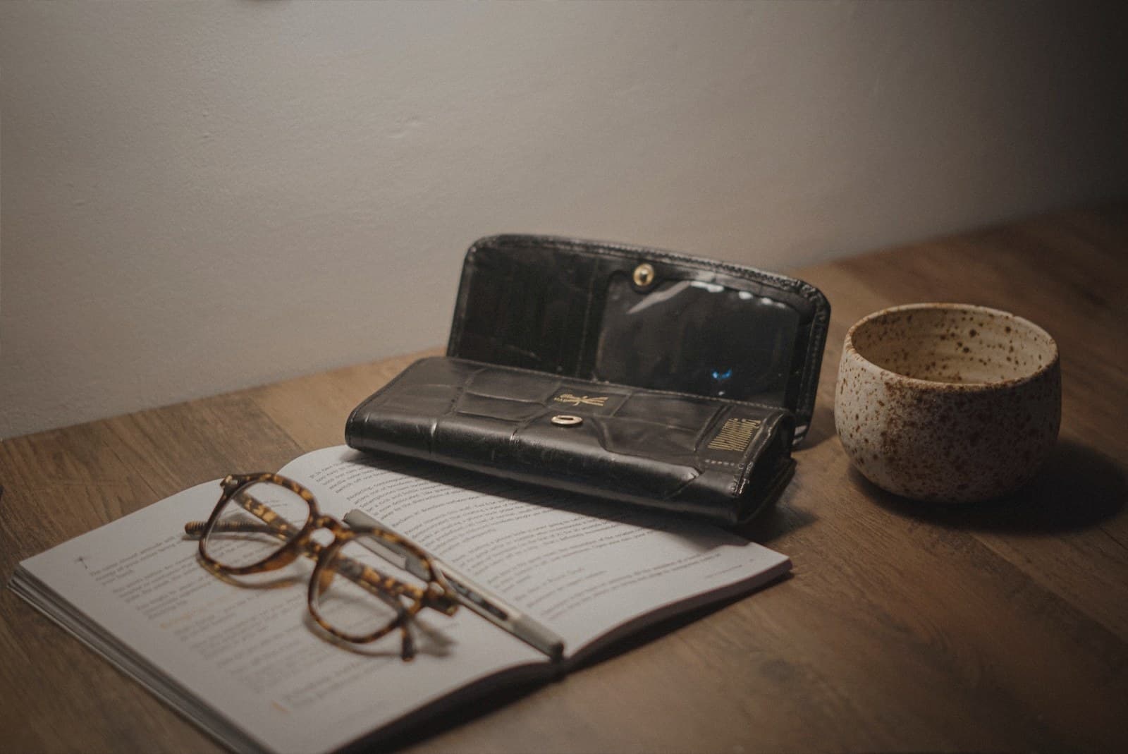 An organized workspace shot from above: reading glasses, a wallet, and a coffee mug arranged on a wooden desk.