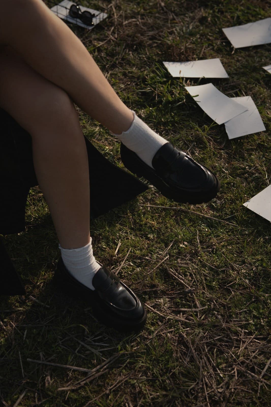 A student in uniform shoes stands on grass outdoors, framed from the knees down.