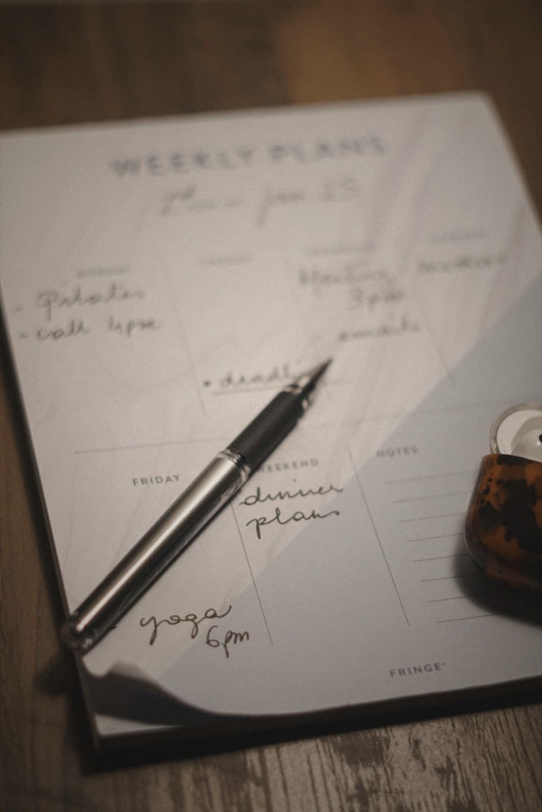A weekly planner open on a wooden desk, handwritten notes and a pen across the spread.