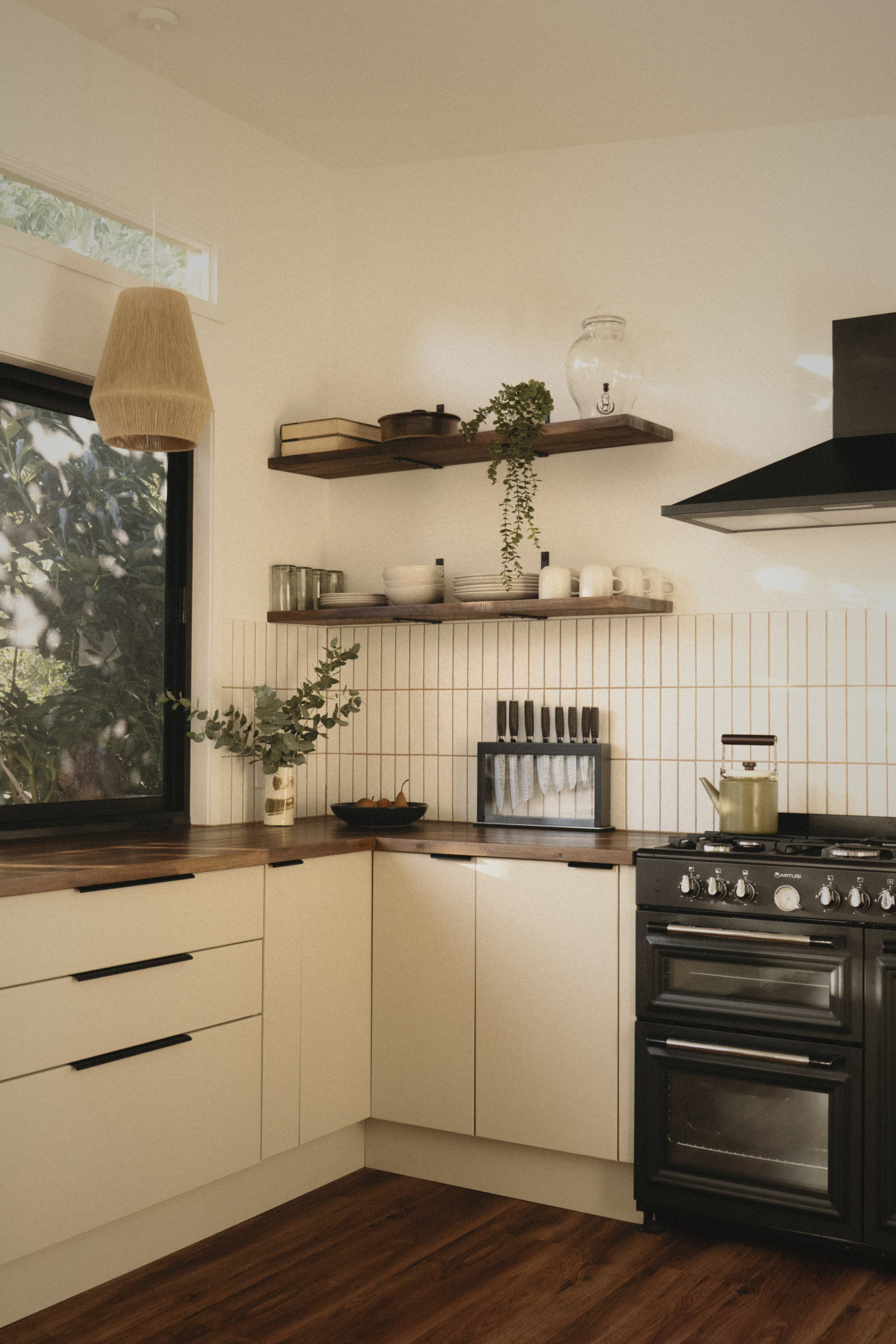 A quiet modern kitchen with cream cabinetry and dark appliances in the soft light of a Sunday morning, before the house has woken up.