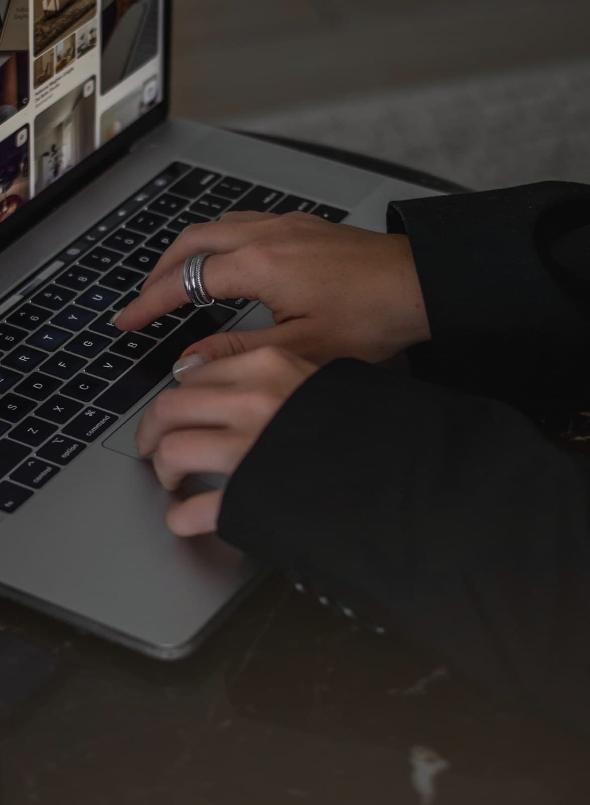 A woman's hands on a laptop keyboard in warm golden-hour light, silver rings on her fingers, deep in intentional work.