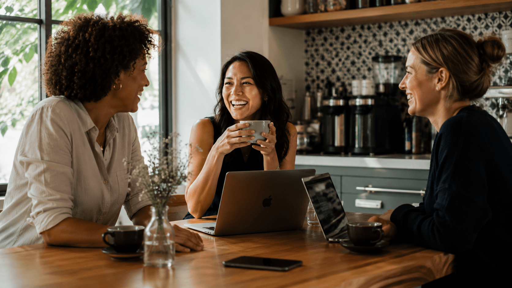 Three working mothers laughing together while running their household workflows on their laptops.