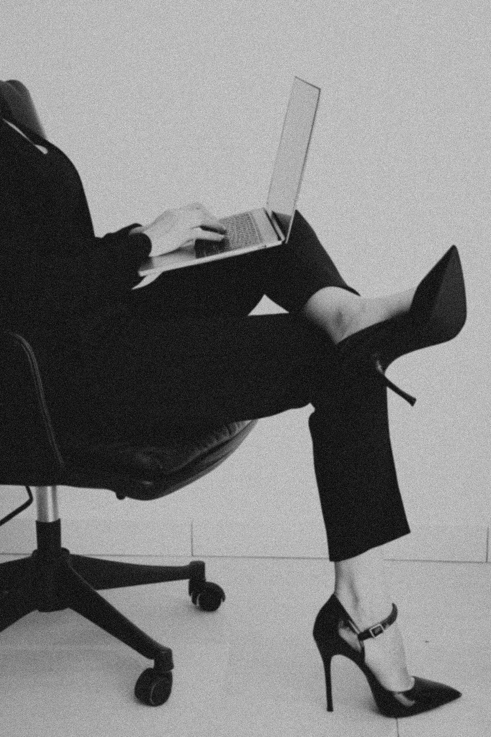 A woman at her laptop in tailored black trousers and stiletto heels