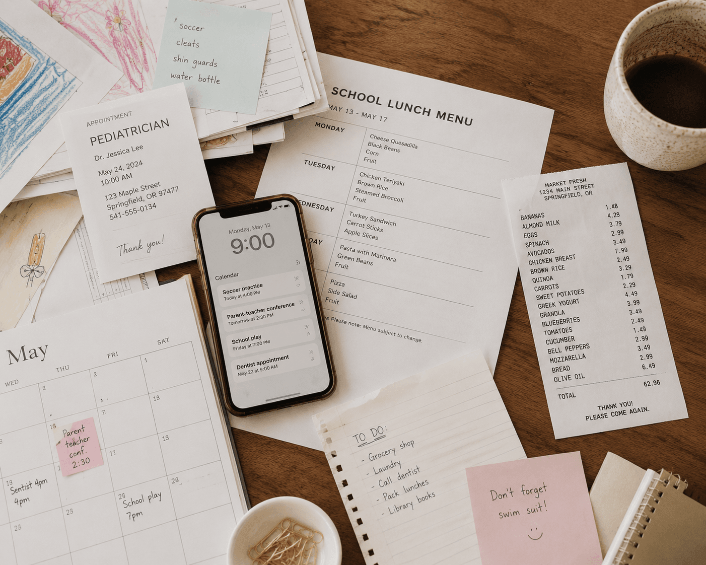 A kitchen table covered in the back-to-school paperwork pile: a school lunch menu, a supply list, a pediatrician card, a wall calendar, and a phone showing the week's events.
