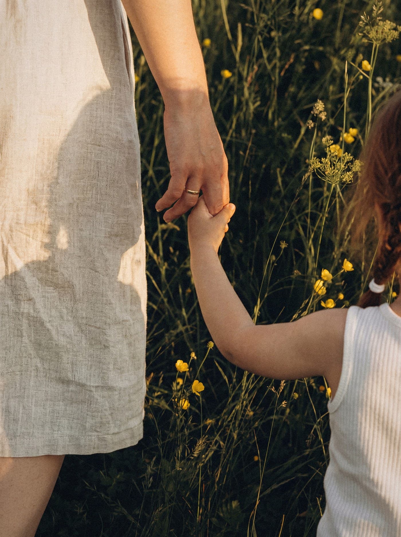 A mother and her child holding hands in a sunlit field