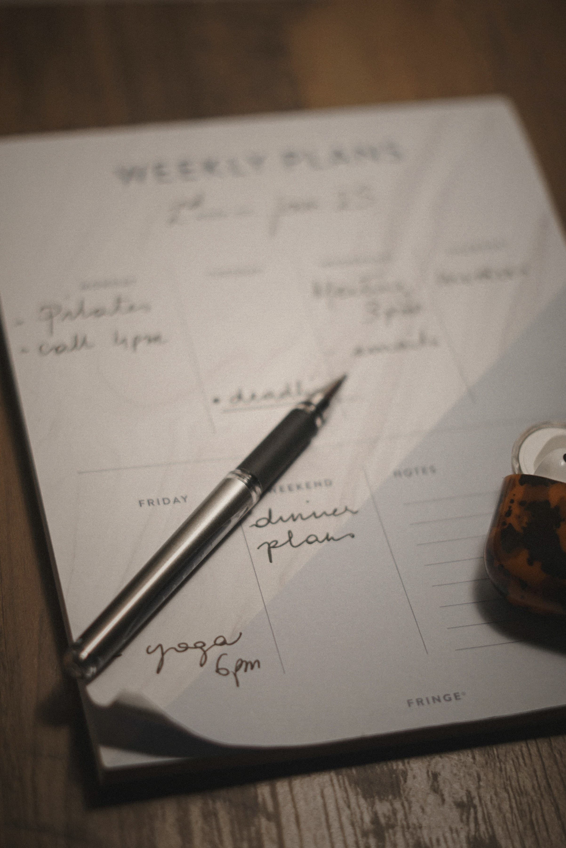 A weekly planner on a wooden desk, handwritten notes and a fountain pen resting across the page in warm afternoon light.