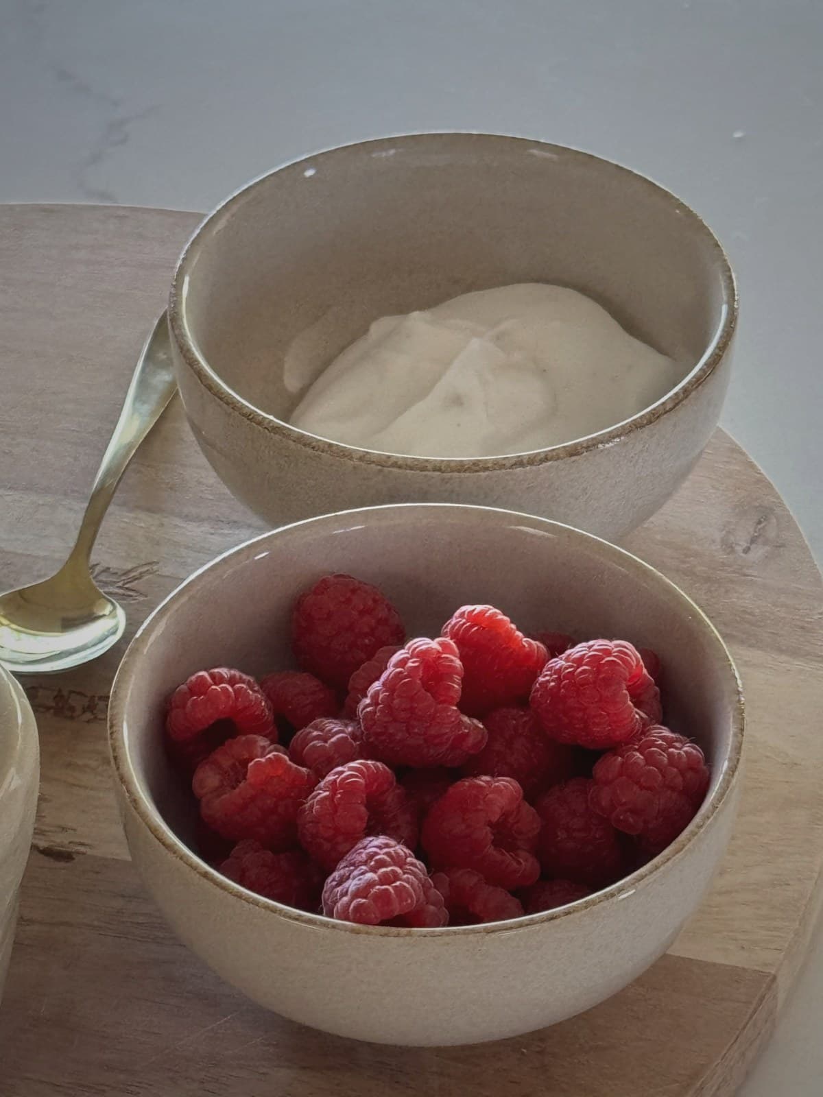 Fresh raspberries and cream in two minimalist ceramic bowls on a pale countertop.