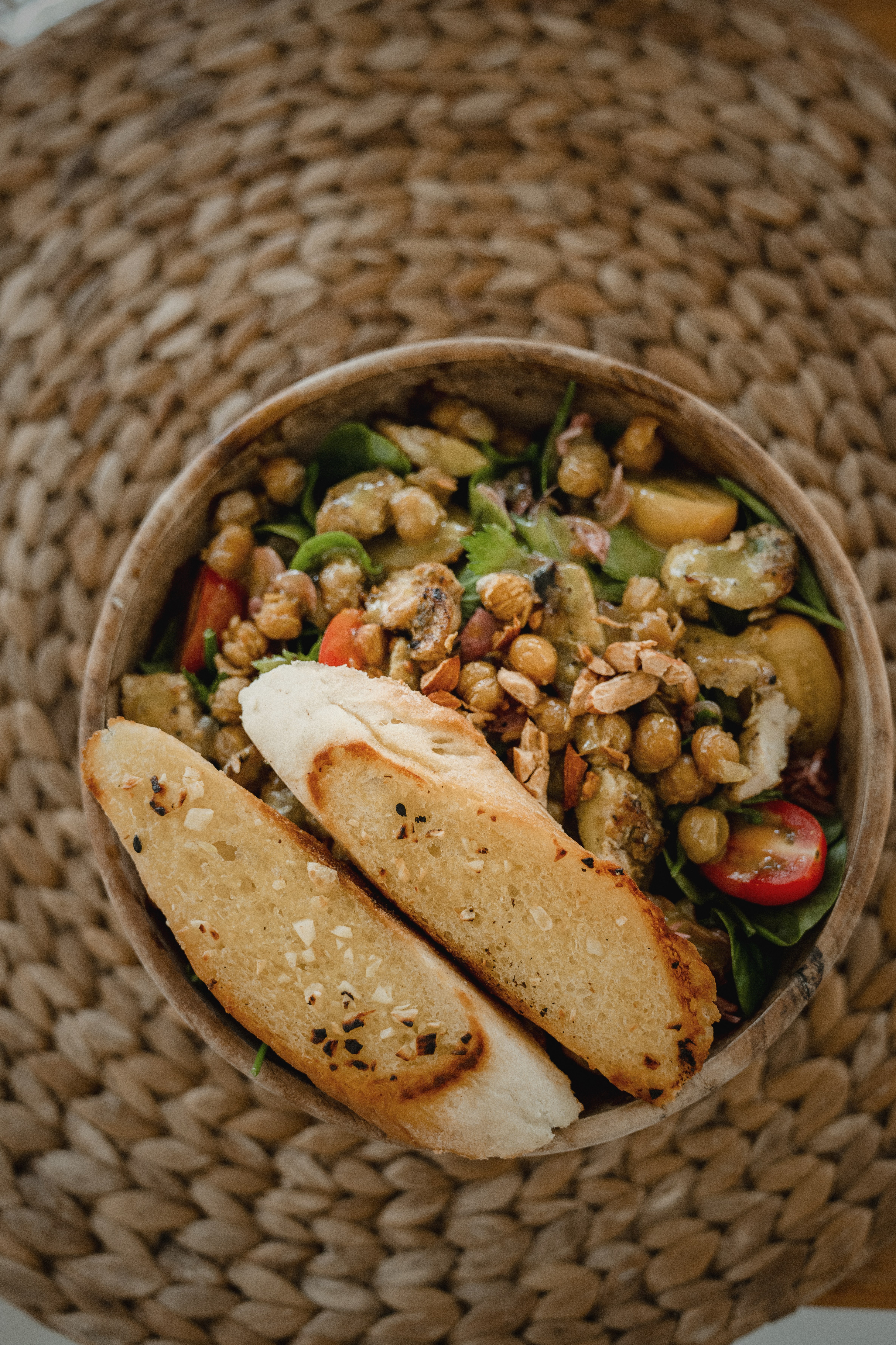 An overhead shot of a nourishing lunch bowl with roasted vegetables, legumes, and fresh bread on a linen surface.