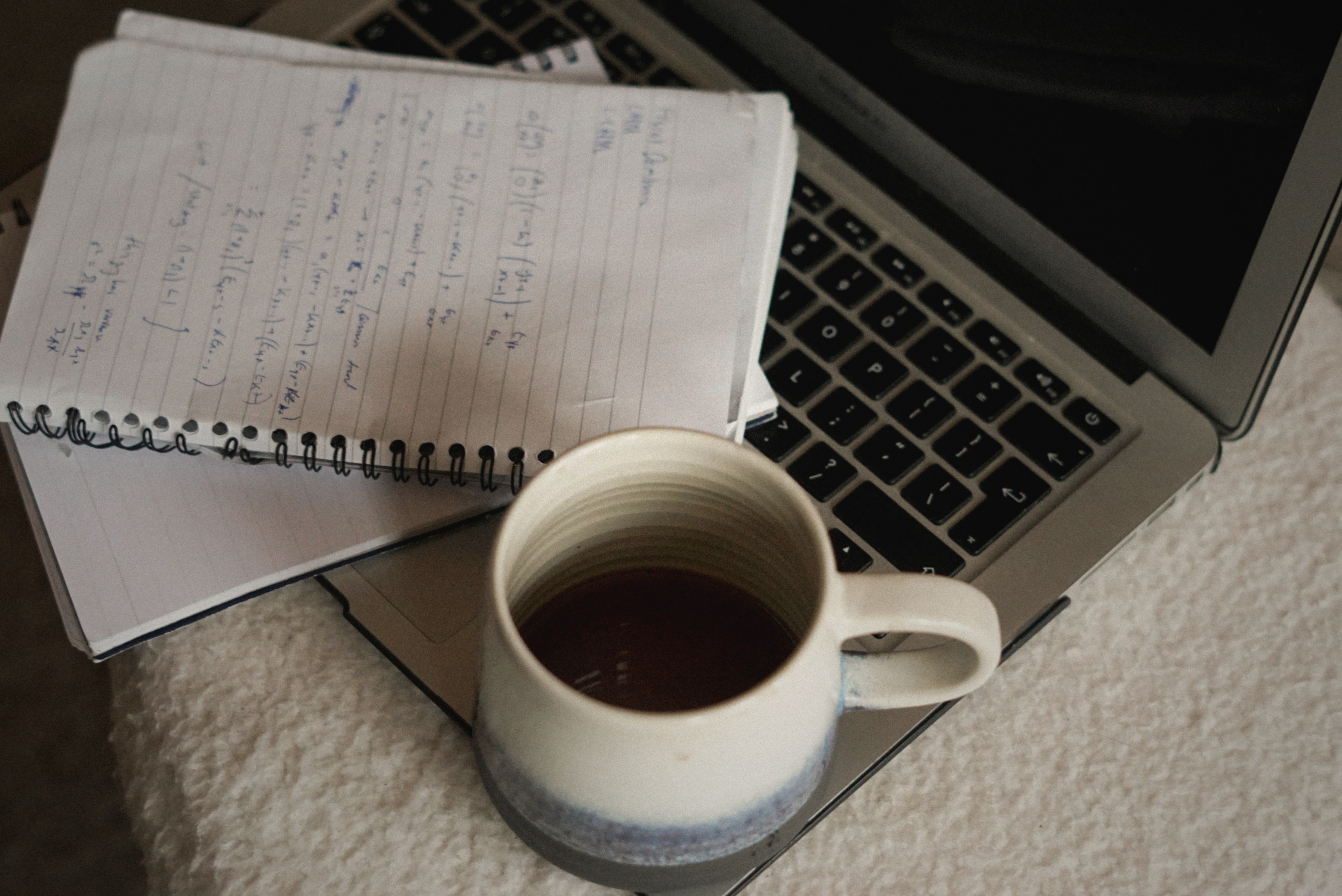 A clean wooden workspace with a warm cup of coffee, a small notebook, and a phone with a handwritten list resting beside it.